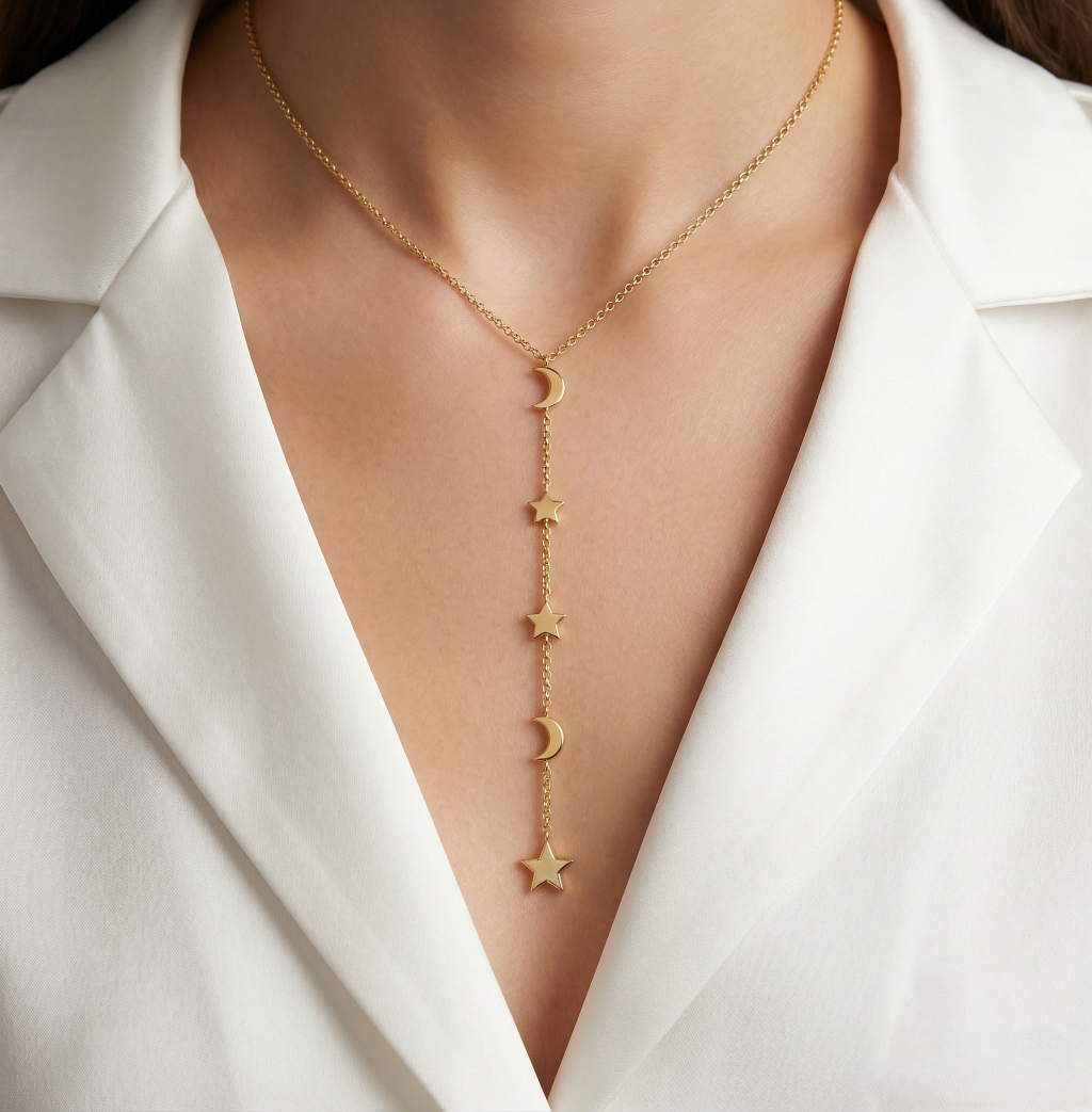 Gold necklace with star and moon pendants on a person wearing a white blazer.