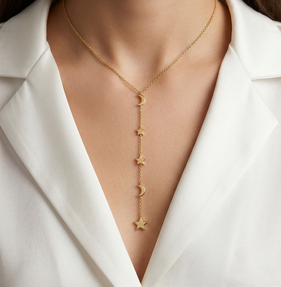 Gold necklace with star and moon pendants on a person wearing a white blazer.