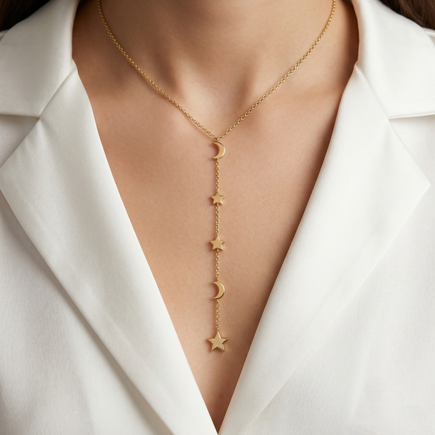 Gold necklace with star and moon pendants on a person wearing a white blazer.