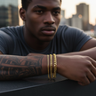 Man with tattoos and gold bracelets against a cityscape background