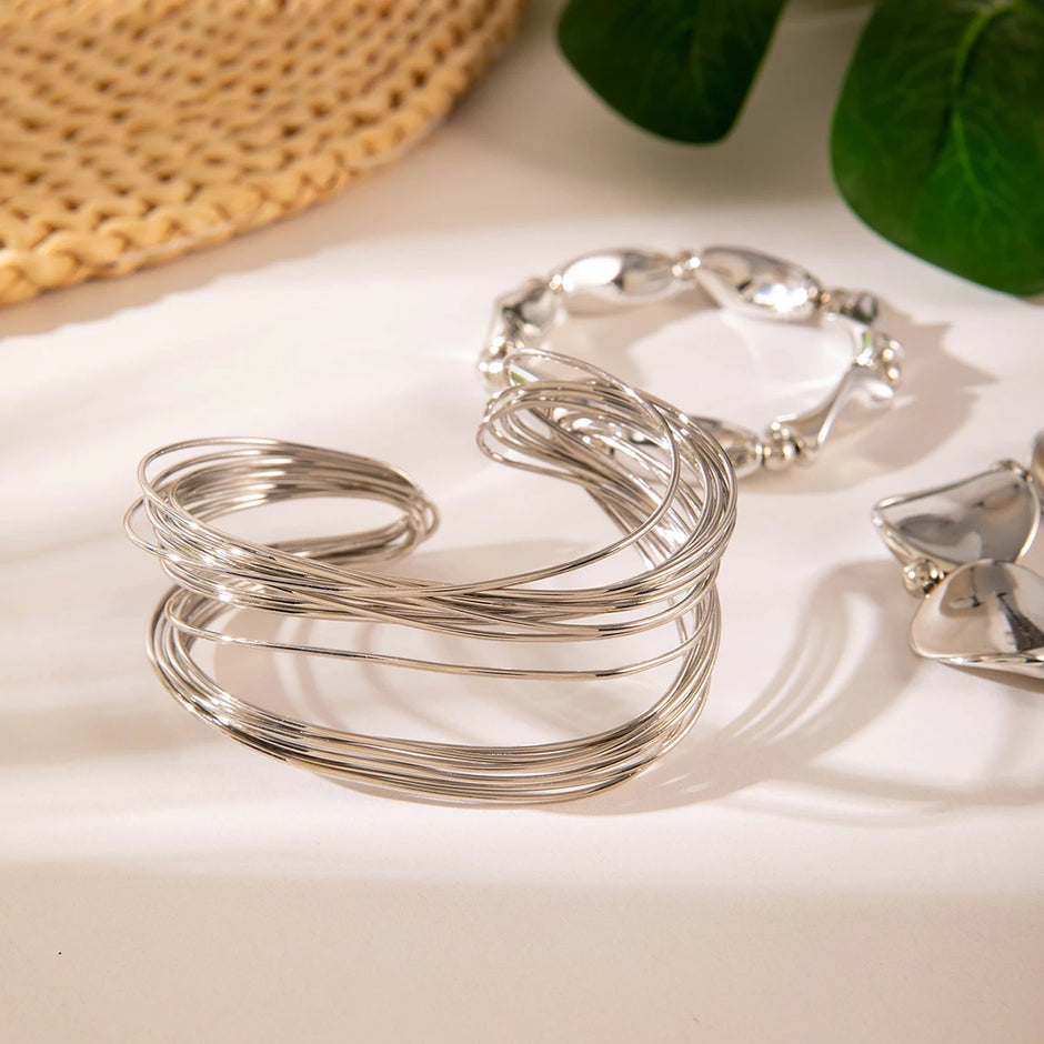 Silver bracelets on a light surface with a woven mat and green leaves in the background
