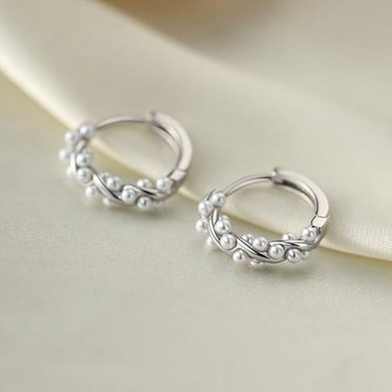 Silver hoop earrings with pearl-like beads on a beige fabric background