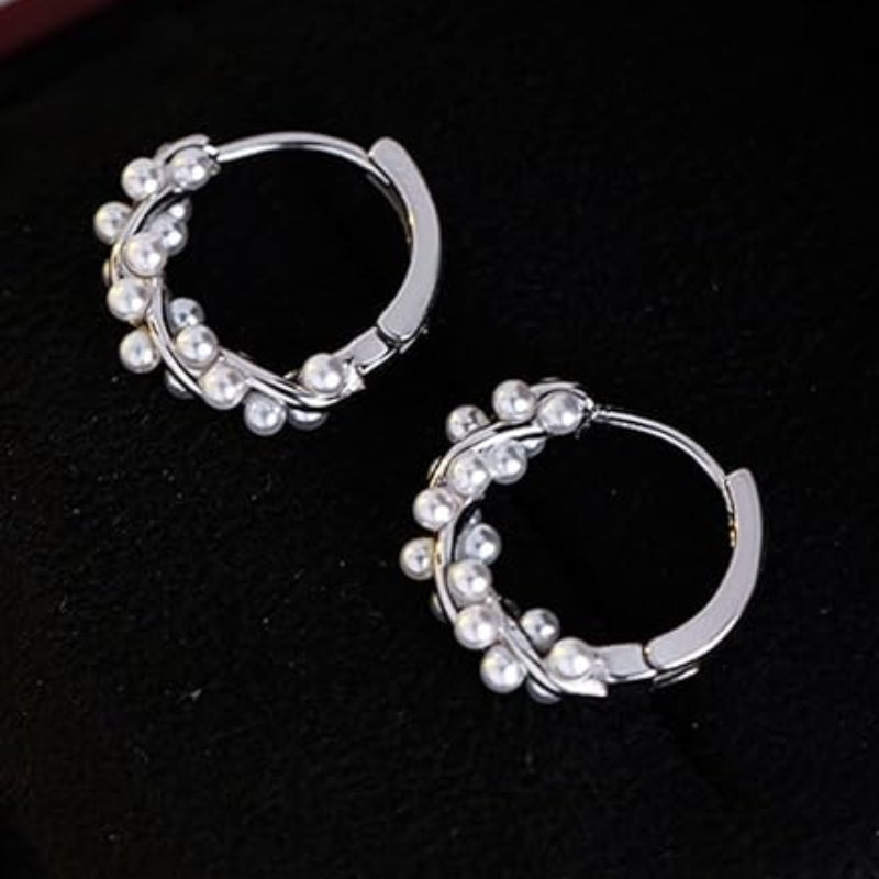 Silver hoop earrings with pearl-like beads on a dark surface