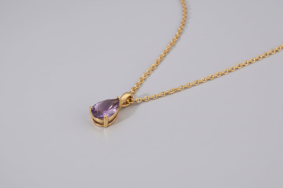 Gold necklace with a purple teardrop pendant on a white background