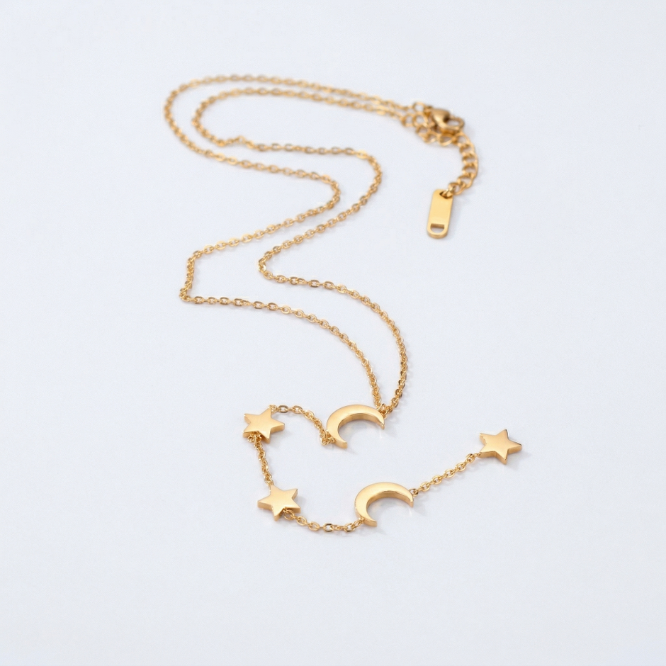Gold necklace with star and moon charms on a light gray background
