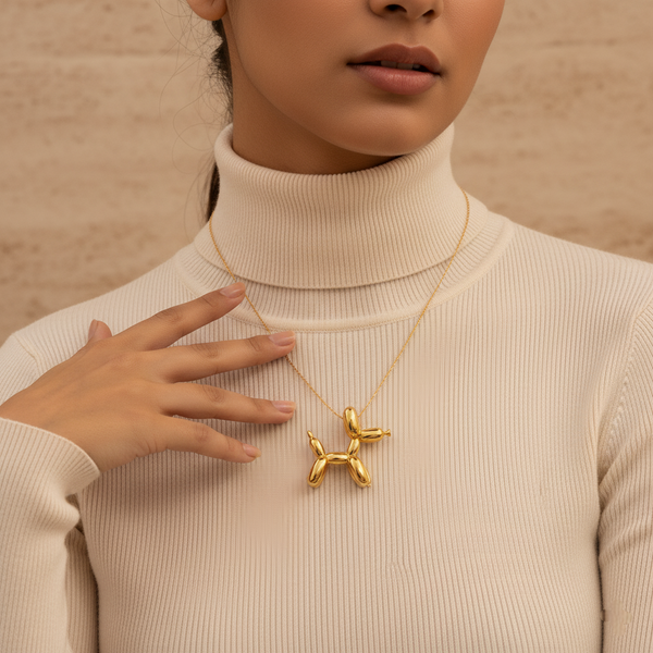 "A person wearing a white turtleneck sweater and a gold necklace with a shiny, balloon dog pendant.