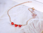 Anklet with red beads and a gold chain on a white background