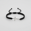 Black braided bracelet with a silver cross charm on a light gray background