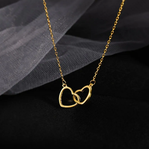 Close-up of interlocking hearts pendant necklace showing two intertwined hearts in titanium steel with high-polish finish. Romantic love jewelry design.