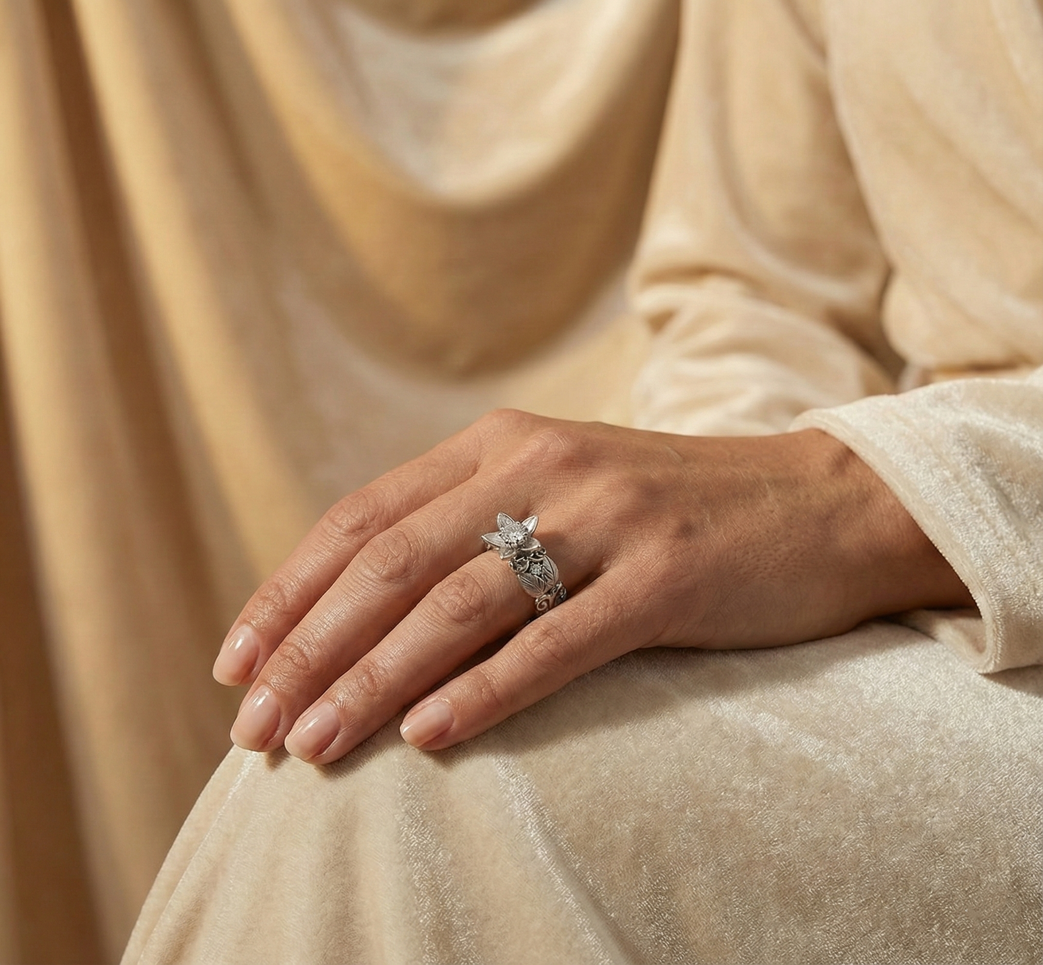 Hand wearing a silver Flower Proposal Ringon a beige fabric background