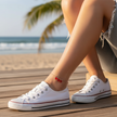 An anklet with red beads and a gold chain worn by a person sitting on a wooden deck by the beach.