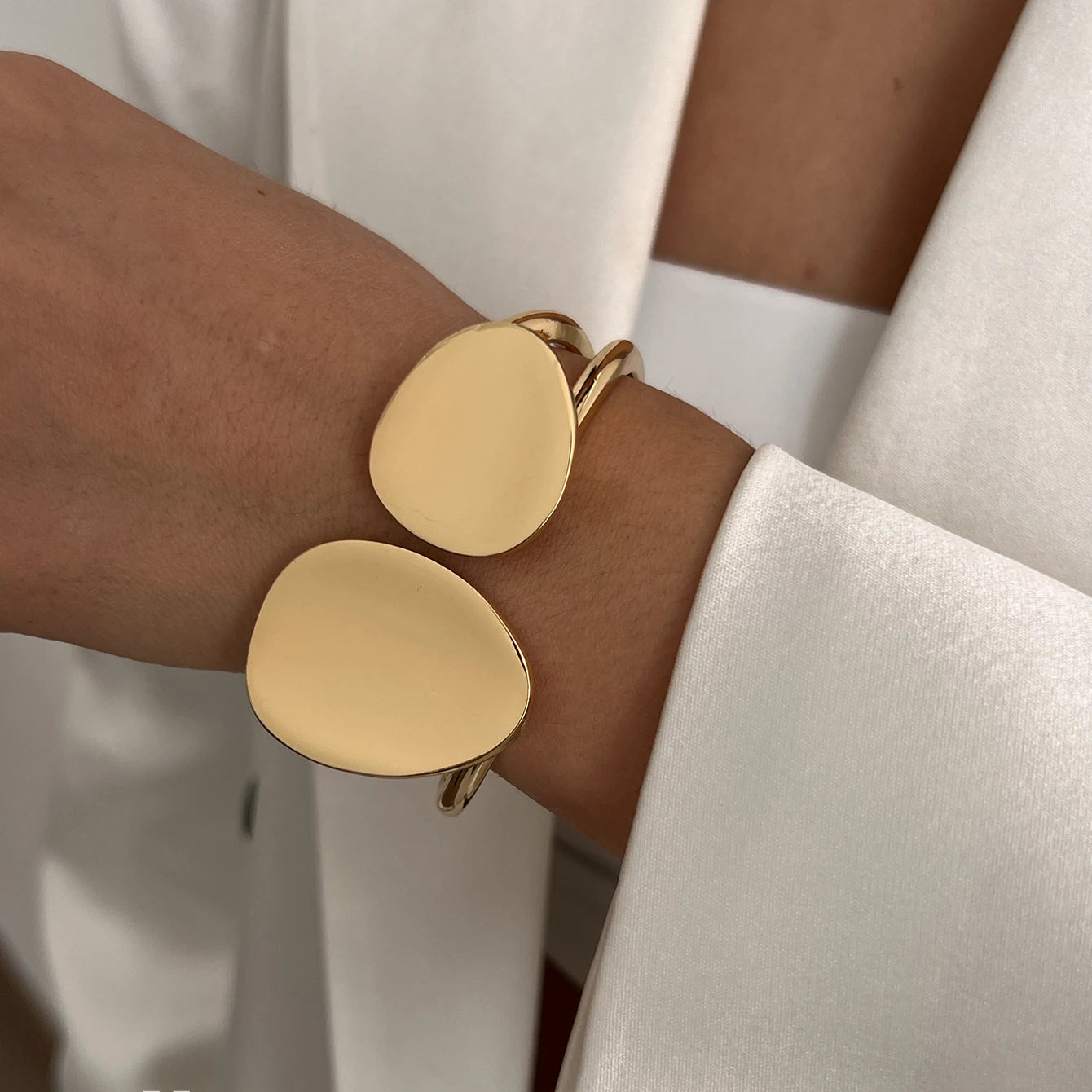 Gold bangle with two oval links on a wrist with a neutral background