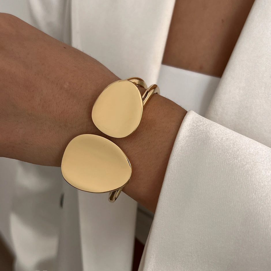 Gold bangle with two oval links on a wrist with a neutral background