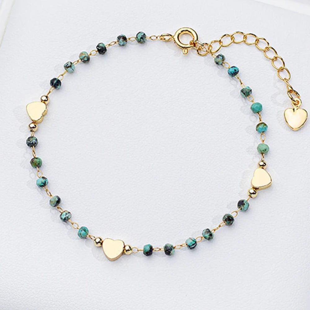 Gold bracelet with heart-shaped charms and green beads on a white surface