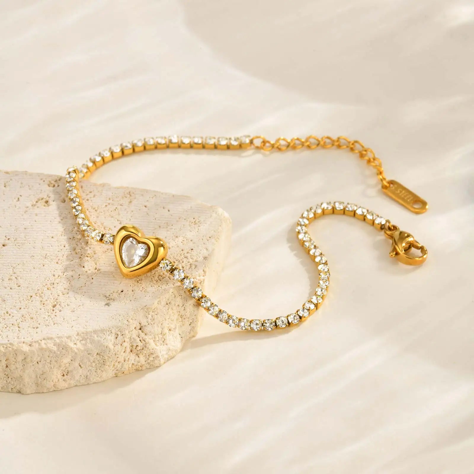 Gold bracelet with heart-shaped clasp on a beige stone surface