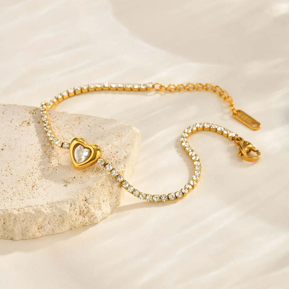 Gold bracelet with heart-shaped clasp on a beige stone surface