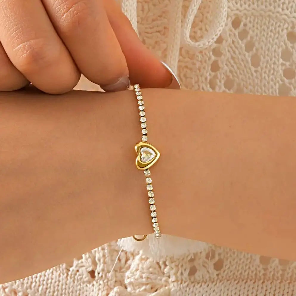 Gold heart-shaped bracelet with clear stones on a wrist against a textured beige background
