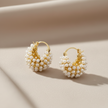 Gold hoop earrings with pearl-like beads on a beige background