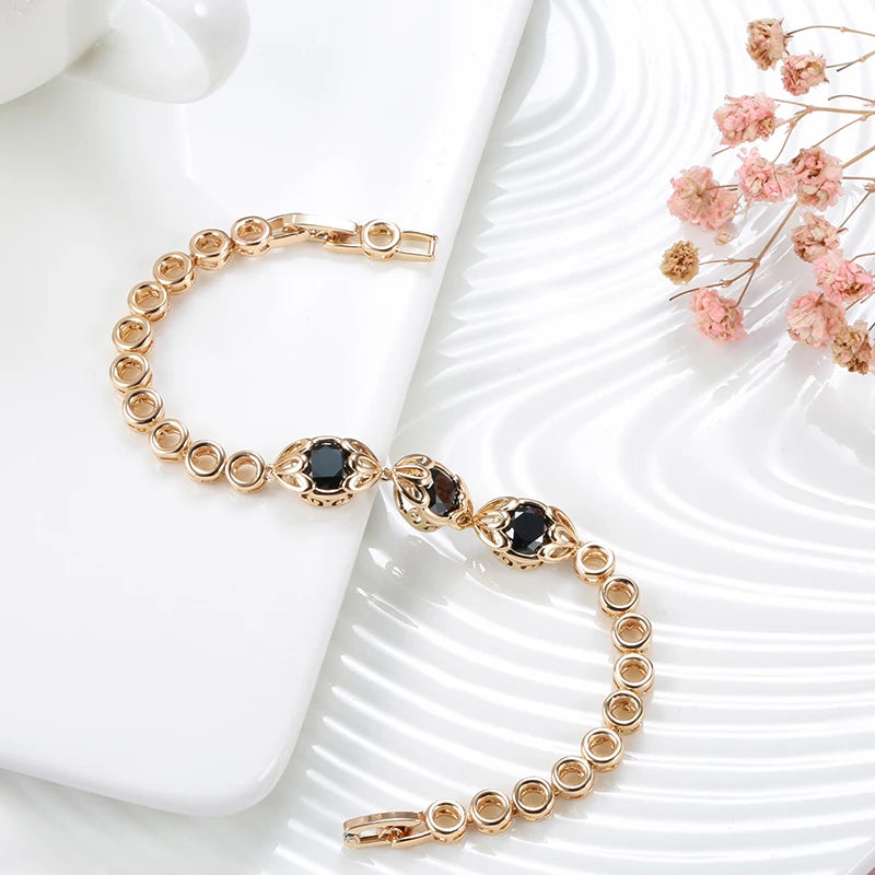 Gold bracelet with black stones on a white surface with pink flowers