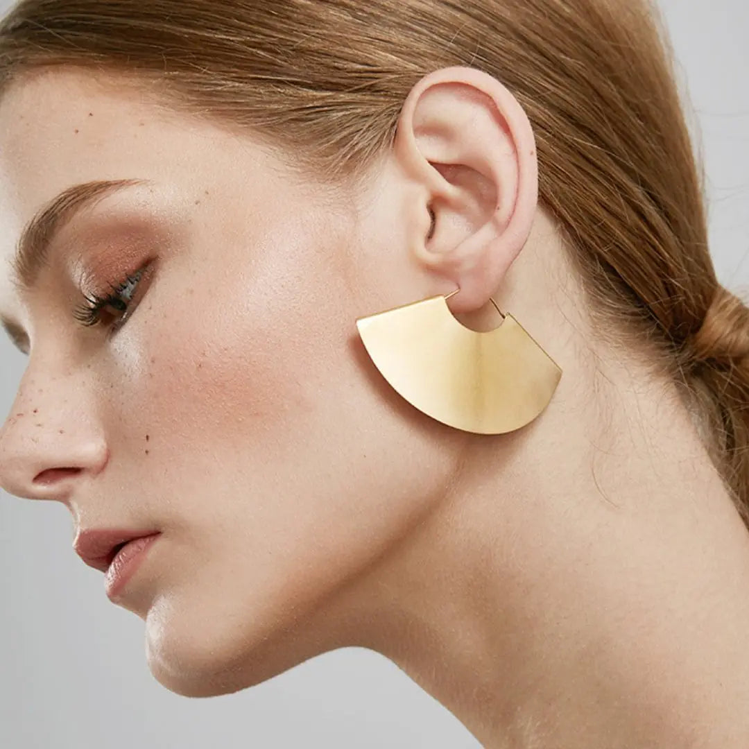 Gold earring worn by a person with a neutral background