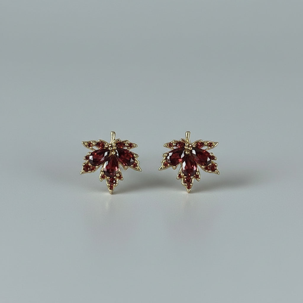 Maple leaf-shaped earrings with red stones on a white textured surface