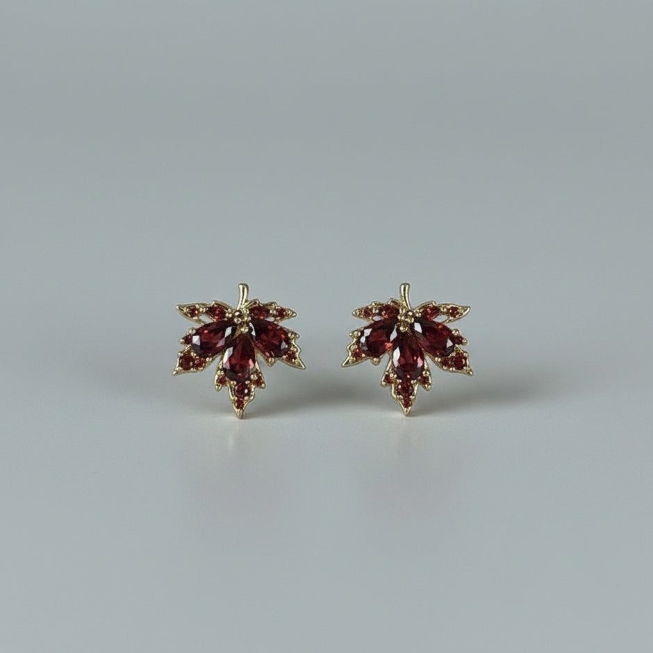 Maple leaf-shaped earrings with red stones on a white textured surface