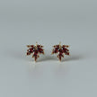 Maple leaf-shaped earrings with red stones on a white textured surface