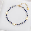 Navy blue beaded bracelet with gold heart charms on a white jewelry box