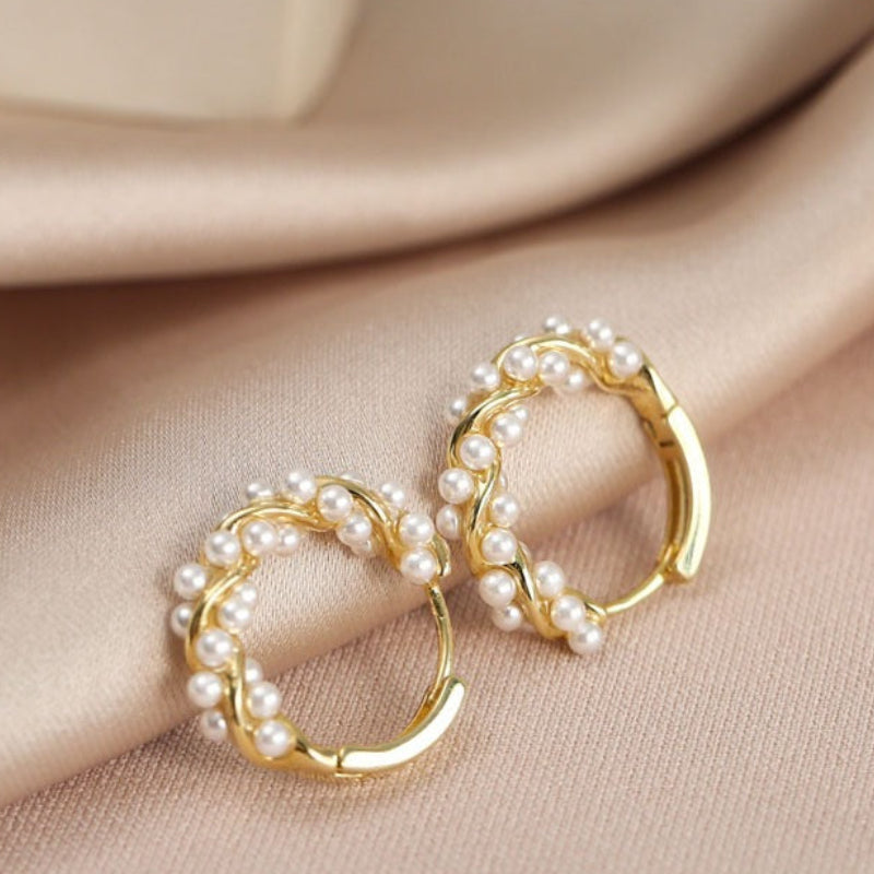Gold hoop earrings with pearl accents on a beige fabric background