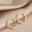 Gold hoop earrings with pearl accents on a beige fabric background