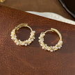 Gold hoop earrings with pearls on a brown leather surface