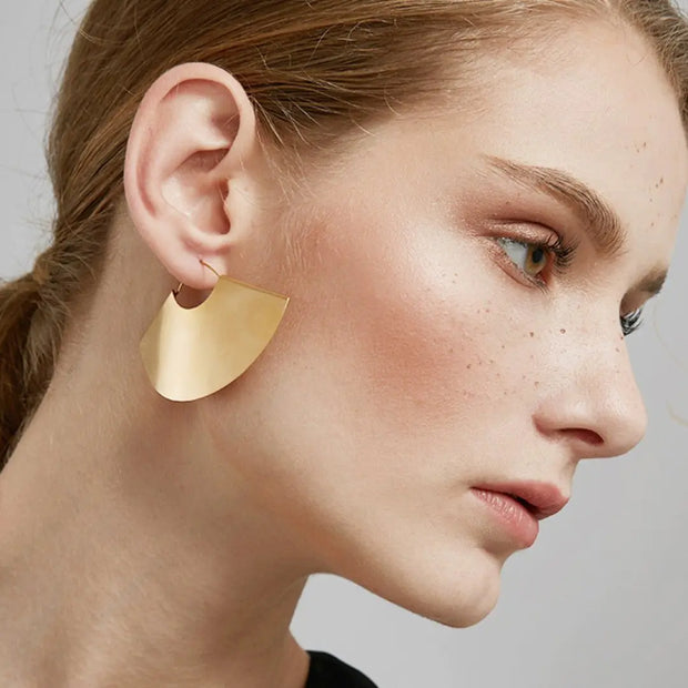 Close-up of a woman wearing gold earrings with a neutral background