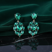 Pair of emerald green earrings on a dark green fabric background