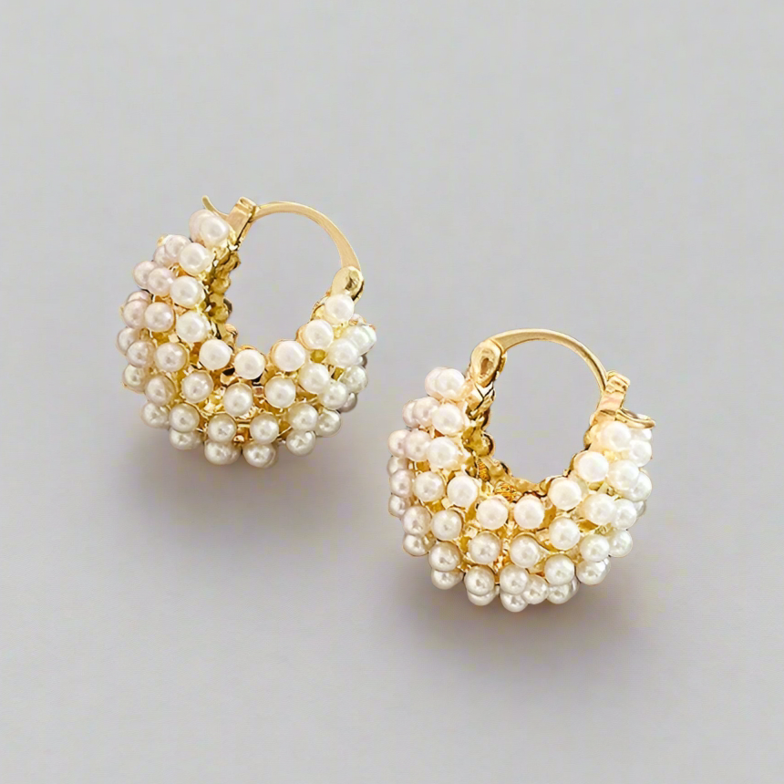 Pair of gold hoop earrings with pearl beads on a light gray background