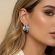 Close-up of a woman wearing silver chunky hoop earrings.  with a neutral background