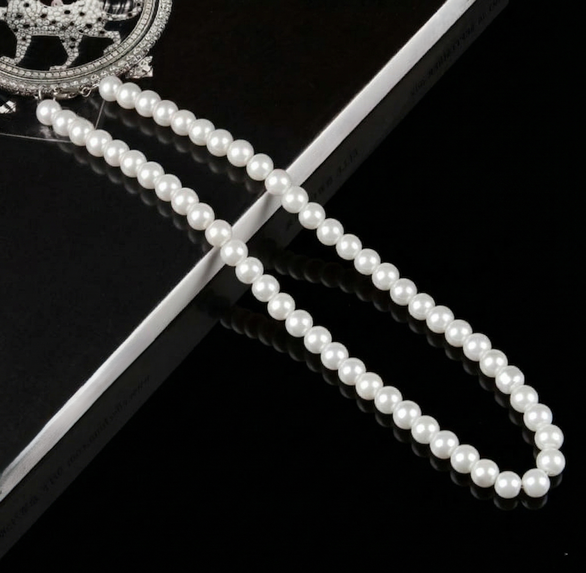 Pearl necklace on a black surface with a decorative brooch.