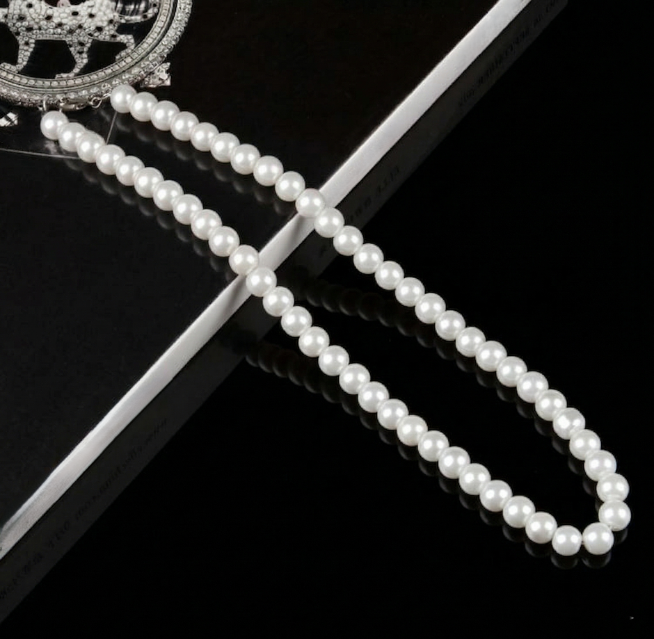 Pearl necklace on a black surface with a decorative brooch.