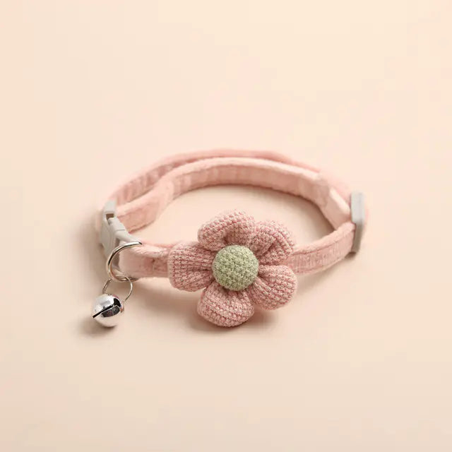 Pink pet collar with a knitted flower and bell on a beige background