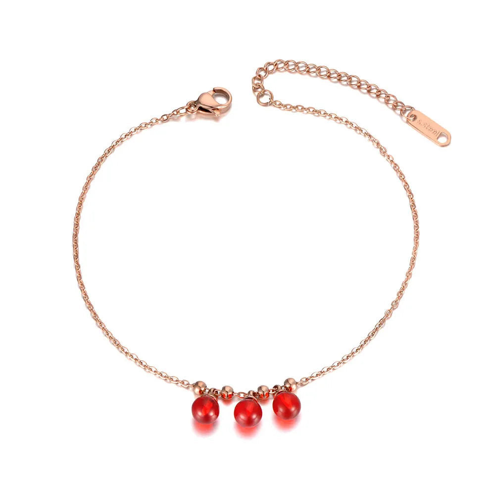 Rose gold anklet with red beads on a white background