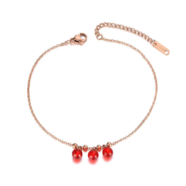 Rose gold anklet with red beads on a white background