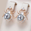 Spider-shaped earrings with pearls and gemstones on a beige background