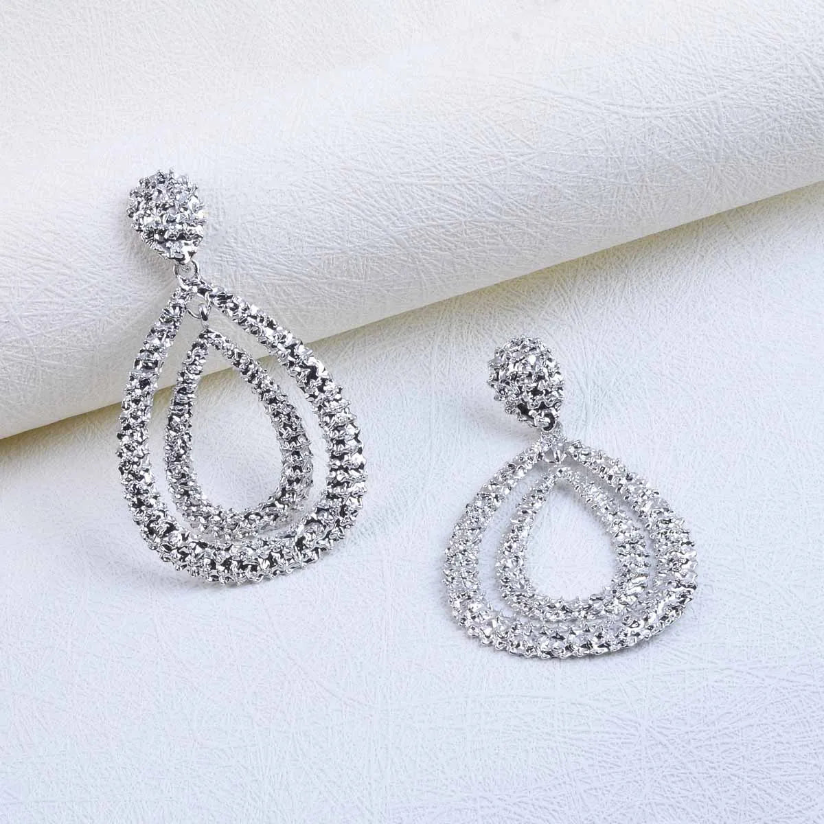 Pair of silver teardrop earrings on a white fabric background