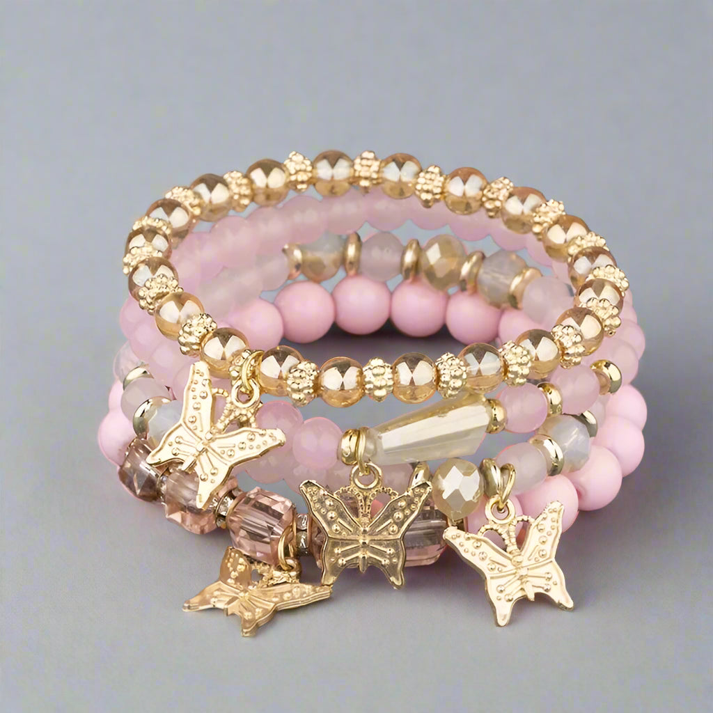 Stack of pink beaded bracelets with gold butterfly charms on a textured surface.