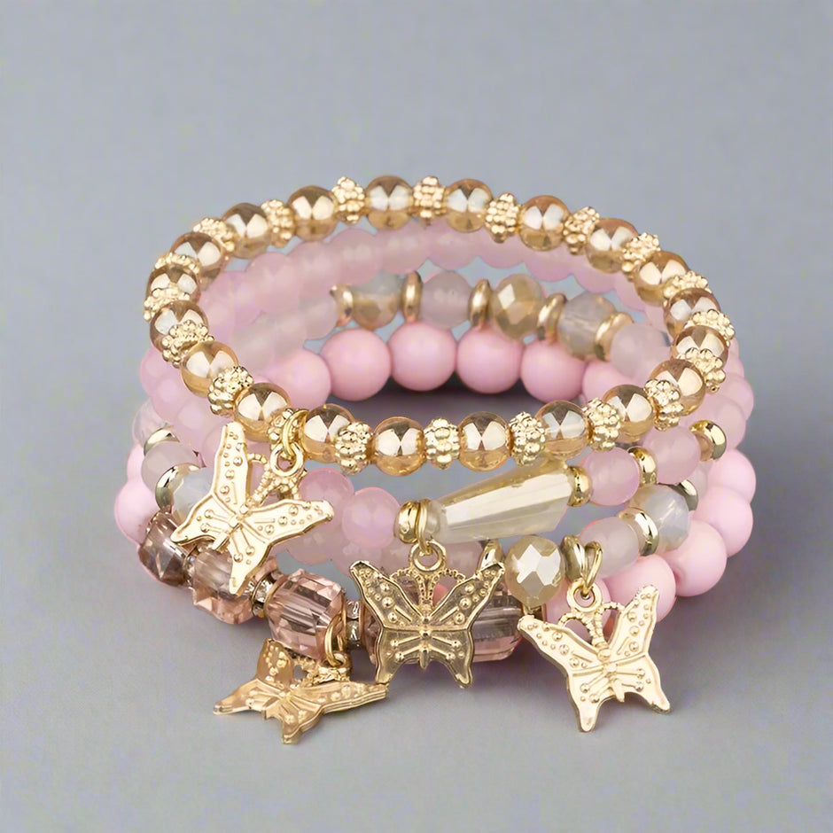 Stack of pink beaded bracelets with gold butterfly charms on a textured surface.