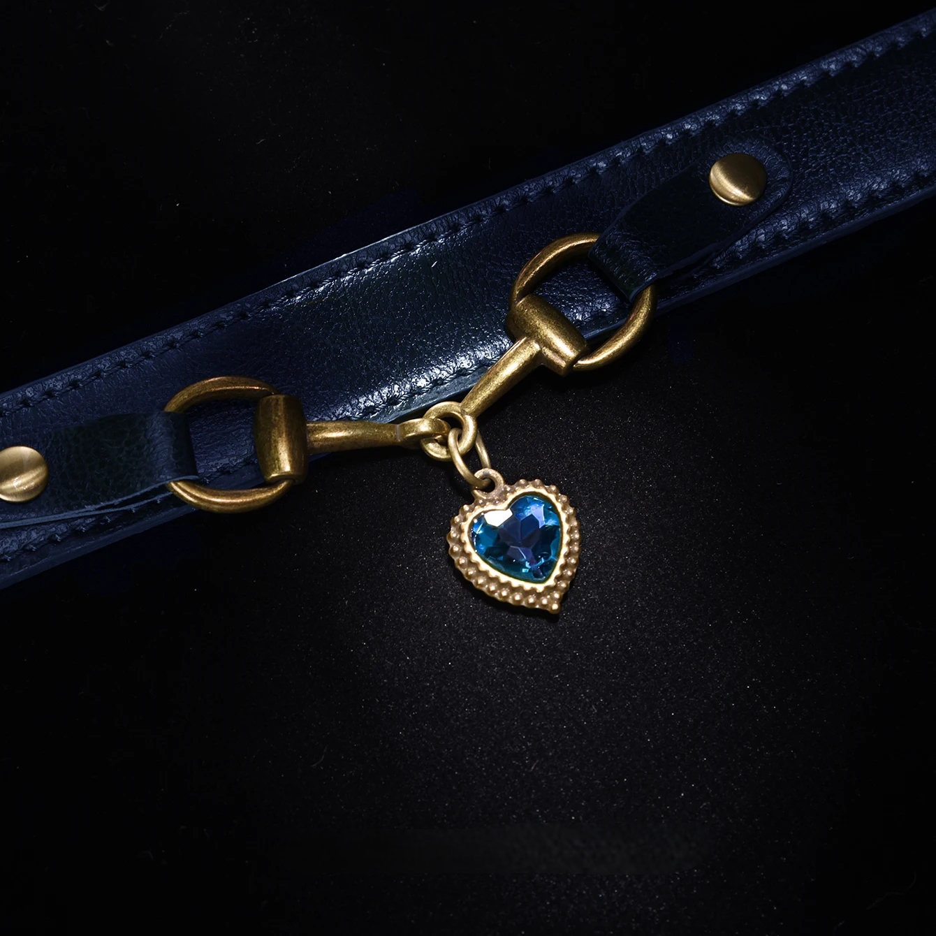 Blue leather strap with a gold clasp and blue heart charm on a black background
