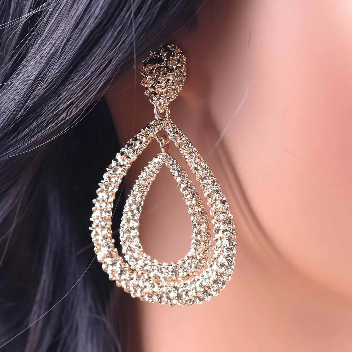 Close-up of a sparkling teardrop earring on an ear with blurred hair and skin in the background.