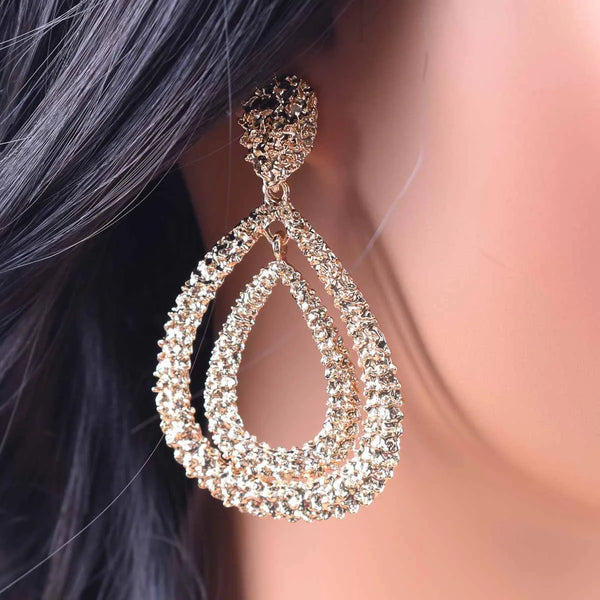 Close-up of a sparkling teardrop earring on an ear with blurred hair and skin in the background.