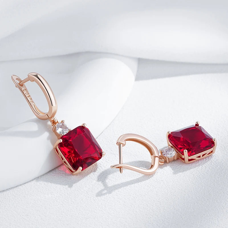 Rose gold earrings with red gemstones on a white fabric background