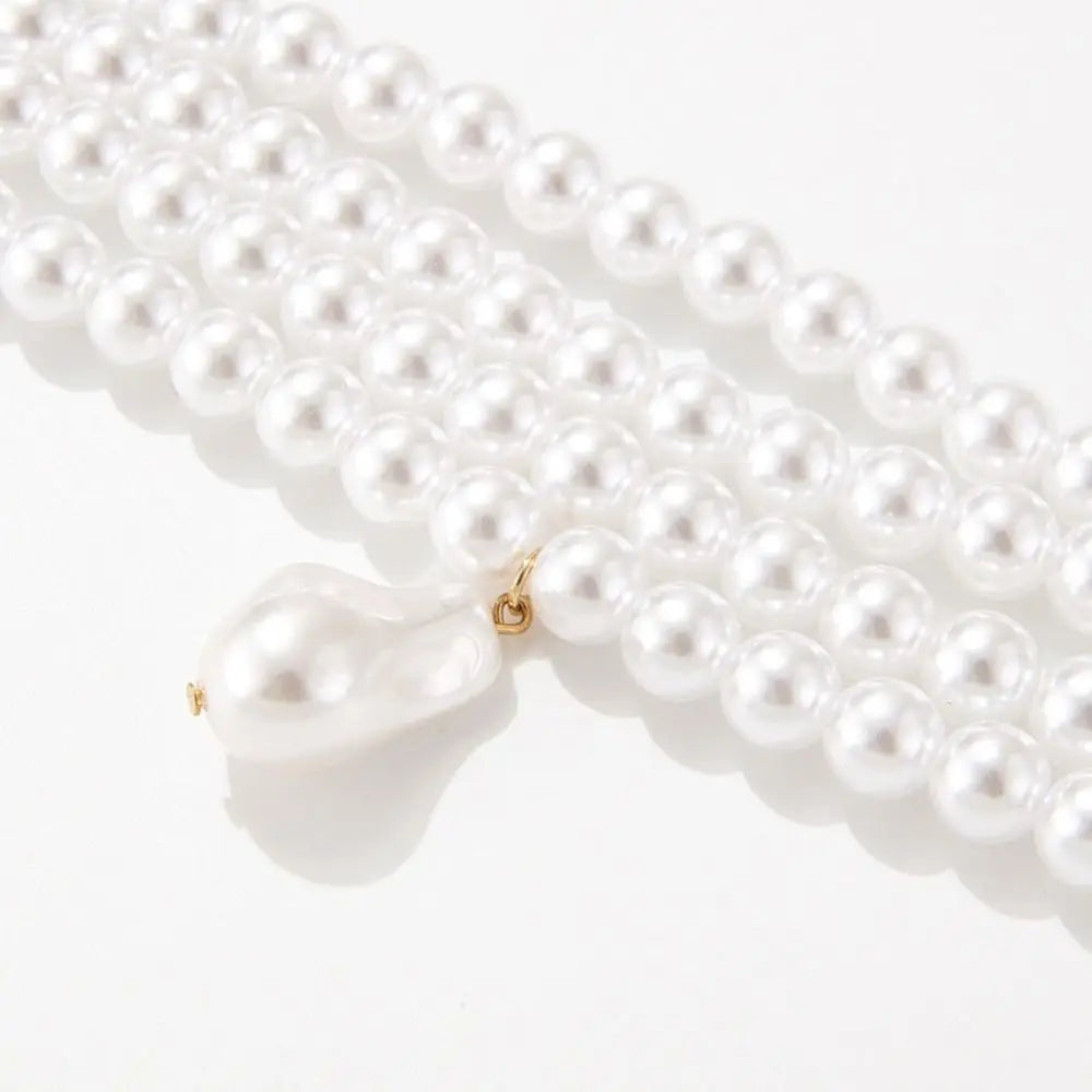 a choker-style necklace made of four rows of small, round white pearls. It has a gold-toned clasp at the back and a single, larger, teardrop-shaped white pearl pendant hanging from the center front.