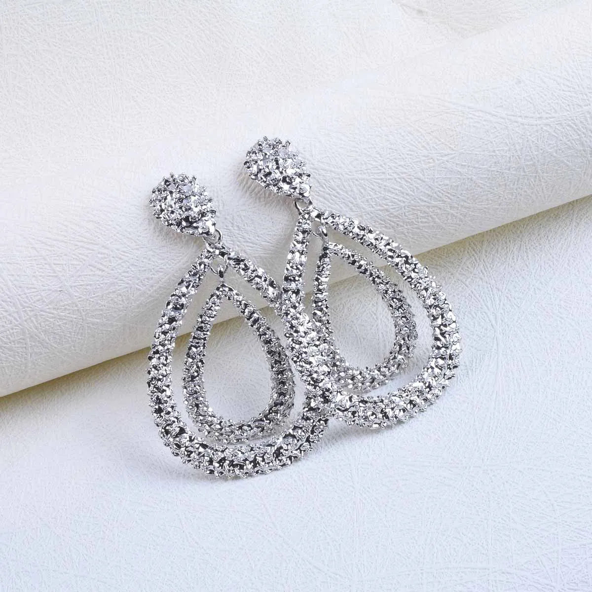 Pair of silver-plated, double teardrop dangle earrings with a textured, rhinestone-encrusted finish. 